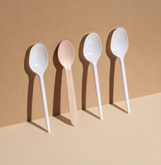 Plastic and wooden spoons on a beige background with shadow. Eco concept, plastic free, food. Creative layout