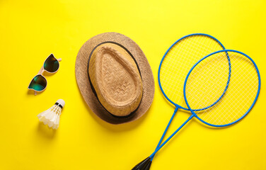 Badbintion racket with a shuttlecock and hat and sunglasses on yellow bright background. Leisure. Flat lay