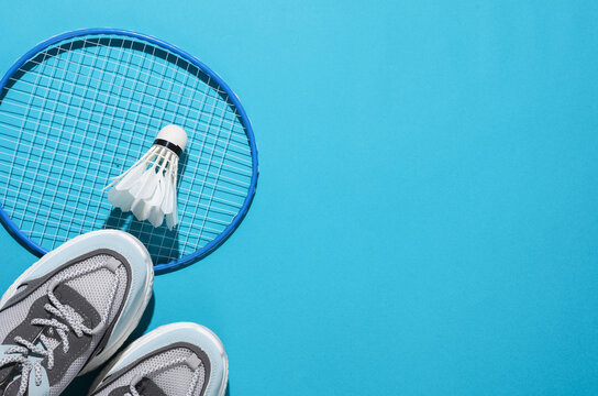 Badbintion racket with a shuttlecock and sneakers on blue bright background. Leisure, copy space