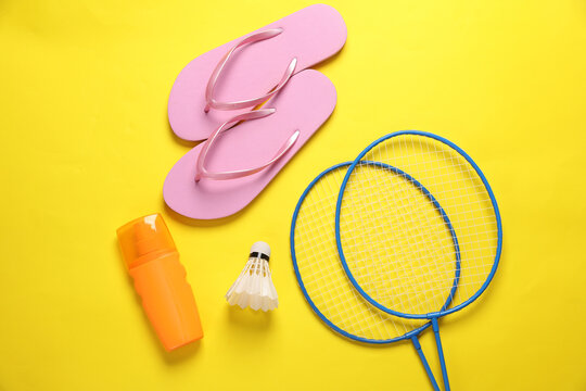 Beach vacation. Badbinton racket, shuttlecock, flip flops, sunblock on yellow background with shadow. Flat lay