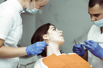 Dentist with assistant examines the oral cavity of female patient in dental clinic. Visit to the...
