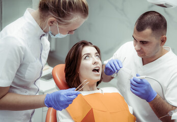 Obraz premium Young woman with open mouth prepares to drill a tooth by the dentist with an assistant at the dental clinic. Dental treatment concept