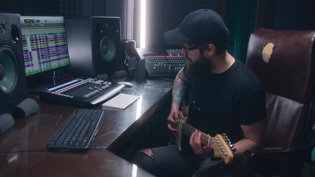 Sound engineer, musician plays electric guitar, records melody for creating new song. Computer screen showing DAW software interface with sound tracks. Professional recording studio. Music production.