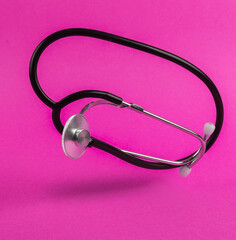 Levitating medical stethoscope on pink background with shadow