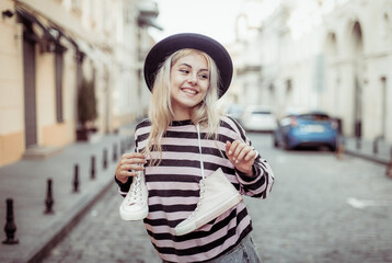 Street fashion. Young trendy girl in stylish clothes holds sneakers in the city