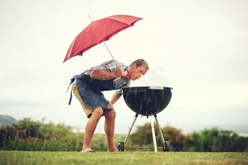 Umbrella, rain and a man outdoor to barbecue food for cooking or insurance in the winter season. Storm, weather and grill with a male person getting wet while trying to bbq on a grass lawn or garden