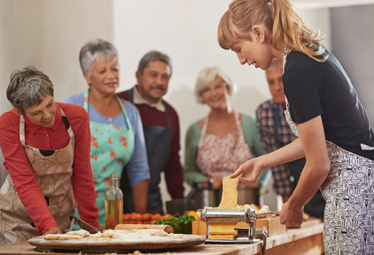 Food, senior cooking class and a woman teaching people in the kitchen of a home for meal preparation. Pasta maker, equipment and learning with mature friends watching a female chef follow a recipe