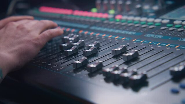 Close up hands shot of sound engineer using mixing console, remote control for adjusting sound, audio mixer. Musician changes the volume level, creates music. Sound recording studio. Music production.