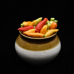 closeup shot of fresh organic hot chili peppers in red, orange and yellow colors stored in a traditional pot jar isolated in a black background