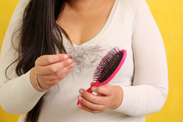 Woman's hands take a hairbrush with many fallen hairs after brushing for alopesia, anemia or...