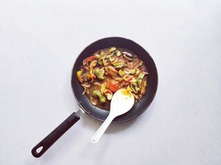 Bell pepper curry in a cooking pan with spoon. Capsicum sauce seasoning. Vegan recipe. White background.