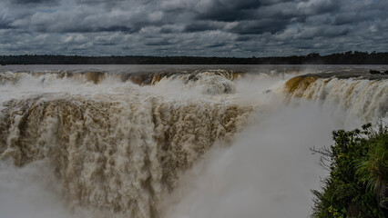 Powerful streams of water are bubbling and foaming, collapsing into the abyss. Spray and mist in the air. Cloudy. Iguazu Falls. The devil's throat. Argentina