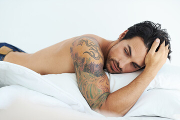 Thinking, relax and shirtless with a sexy man lying on a bed in studio on a white background....