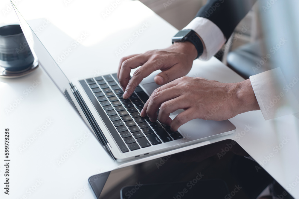 Wall mural Businessman working on laptop computer on white table at office. Business man hands typing on laptop, online working, surfing the internet, close up