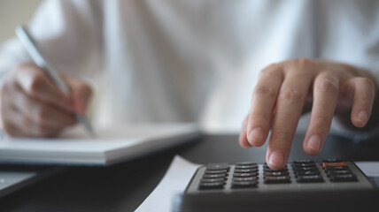 Fototapeta premium Businesswoman working at office, using calculator to calculate financial report, sales data, with laptop computer and business document on office table. Business, finance and investment concept