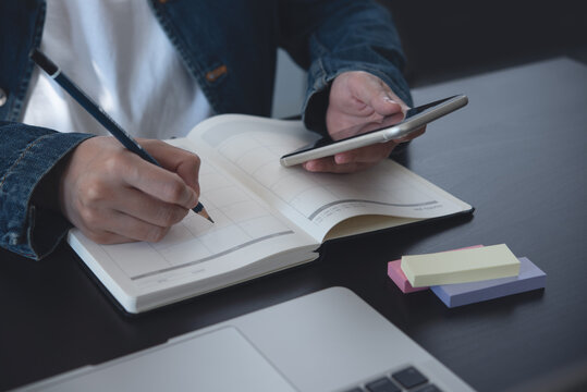 Event planner timetable agenda plan on year 2023 schedule event. Business woman checking planner on mobile phone, taking note on calendar desk on office table. Calendar event plan, work planning