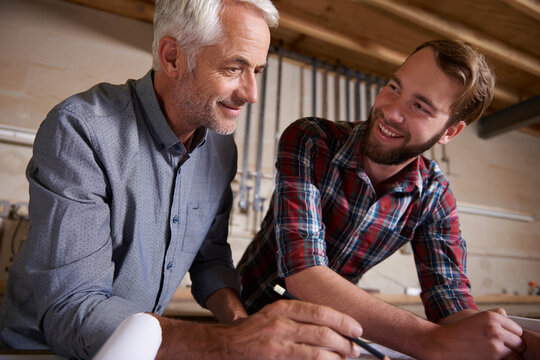 Architecture, teamwork and man with apprentice in workshop for collaboration. Senior engineer, men and smile with trainee, working on remodeling project and drawing plans on paperwork with mentor.