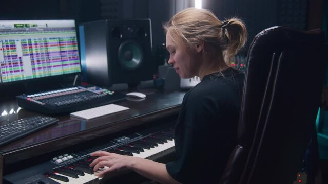 Female sound engineer, musician uses MIDI controller, digital electric piano for creating music. Computer screen shows DAW software interface with sound tracks. Recording studio. Music production.