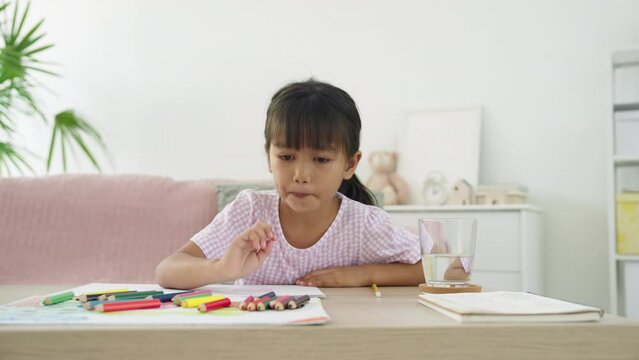 Asian little girl drawing on paper while sitting on floor at home morning