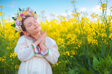Dreaming Beautiful young girl with flower chaplet, ethnic folklore dress with traditional Bulgarian embroidery during sunset on a rapseed agricultural field