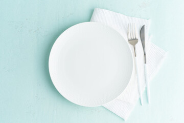 Clean empty white plate, fork and knife on green blue turquoise stone table, copy space, mock up