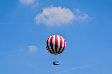 red and white gas filled huge balloon against blue sky in Budapest, city park. white clouds. round metal observation deck with tourists. summer scene. leisure and outdoors. abstract low angle view.  