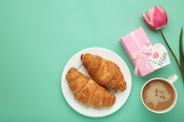 Happy mother's day, beautiful breakfast on mint background, lunch with cup of coffee, fresh croissants, tulip and gift. Spring holiday, family relations.