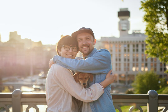Happy couple with a shelter dog hugging in background of the old city in summer. Women with black hair and man in a hat, cute young modern couple with a rescued dog. High quality photo