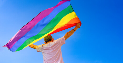mature man holding colorful lgbt rainbow flag raising up into the air the meaning of freedom...
