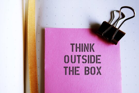 Pink note on notebook with text written THINK OUTSIDE THE BOX , concept of breaking status quo to find innovative solution or create something differently, stand out from the crowd.
