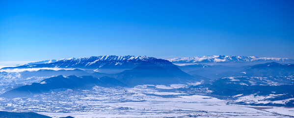 Fototapeta na wymiar Incredible winter landscape of alpine valley under bright sunny light in frosty morning, beautiful alpine panoramic view of snow capped Piatra Craiului and Fagaras mountains in background, Romania