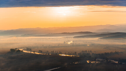 Fototapeta na wymiar Aerial view of the sunrise over the valley in beautiful early morning mist in the highlands. Low clouds and fog cover the sleeping meadow. Hills valley mists landscape. Serene moment in rural area