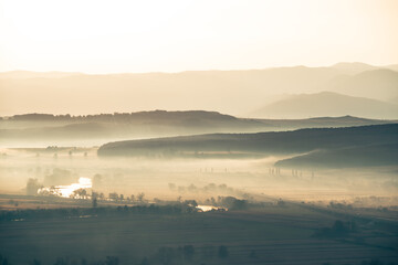 Aerial view of the valley in early morning mist, beautiful in the highlands. Low clouds and fog cover the sleeping meadow. Alpine mountain valley mists landscape at dawn. Serene moment in rural area