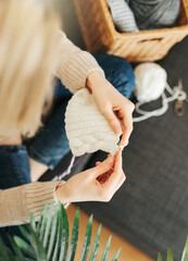 Young woman knitting warm scarf indoors