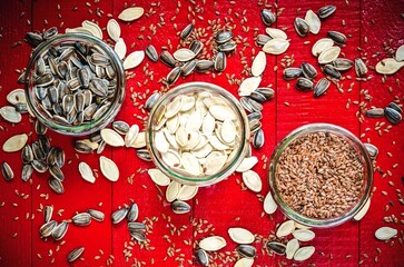 Sunflower, pumpkin and linseed seeds. Healthy food in glass jars on a red wooden table.