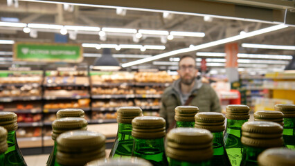 Close-up of many green glass bottles of mineral water on a supermarket shelf and a male buyer standing behind them