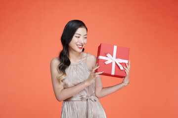 Asian young girl in dress holding red gift box with cheerful expression on background