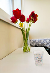 Spring composition with a bouquet of red, yellow and orange tulips with coffee on a white table in the interior of the house.