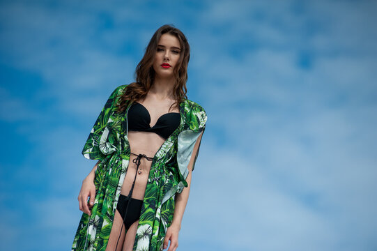 Attractive slender girl in green swimwear posing on white sand beach. Young woman in bikin rests on vacation at sandy ocean shore. Concept travel, swimsuit	