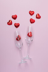 Romantic valentine postcard with two clinking champagne glasses with splash of red heart shaped confetti over pink background. Overhead, top view. Flat design. Valentine's Day concept.
