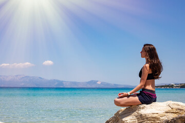 Fototapeta na wymiar Young woman meditating on a rock by the sea on a sunny day. Healthy lifestyle