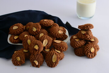 Chocolate almond cookies on a white background with a cup of milk.