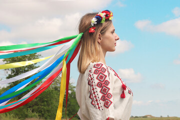 Portrait of Ukrainian young girl in profile in national costume with wreath on her head against background of blue sky
