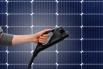 Hand with electric vehicles charging plug on a background of  solar panels