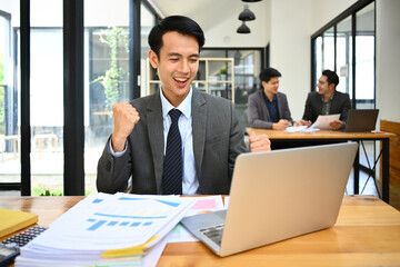 Happy male marketing business manager looking at laptop screen, making winner yes gesture, celebrating business success