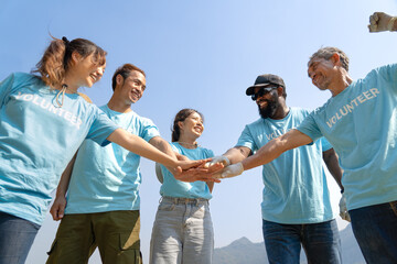 Group of happy multi-ethnic diverse volunteers joining hands stack together and raising hands with...