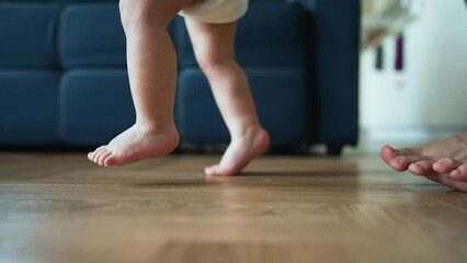 Father helps his son take his first steps on parquet floor. first awkward steps. Tiny legs gain confidence every moment. Joy of a father when he encourages his child to take another step. Happy family