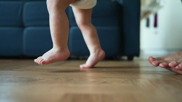 Father helps his son take his first steps on parquet floor. first awkward steps. Tiny legs gain confidence every moment. Joy of a father when he encourages his child to take another step. Happy family
