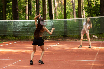 Obraz premium teenager sport outdoor, two girls play badminton in the park in nature on a sunny summer day, badminton competition