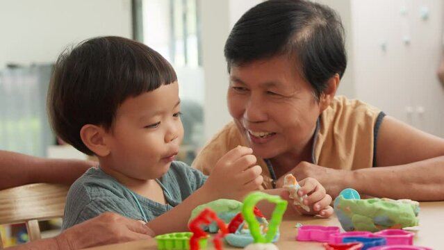 Portrait of Asian Grandmother playing with his Grandson while making toys from plasticine at home. Chinese Senior woman and Little child boy playing dough. Creativity and hobby.	